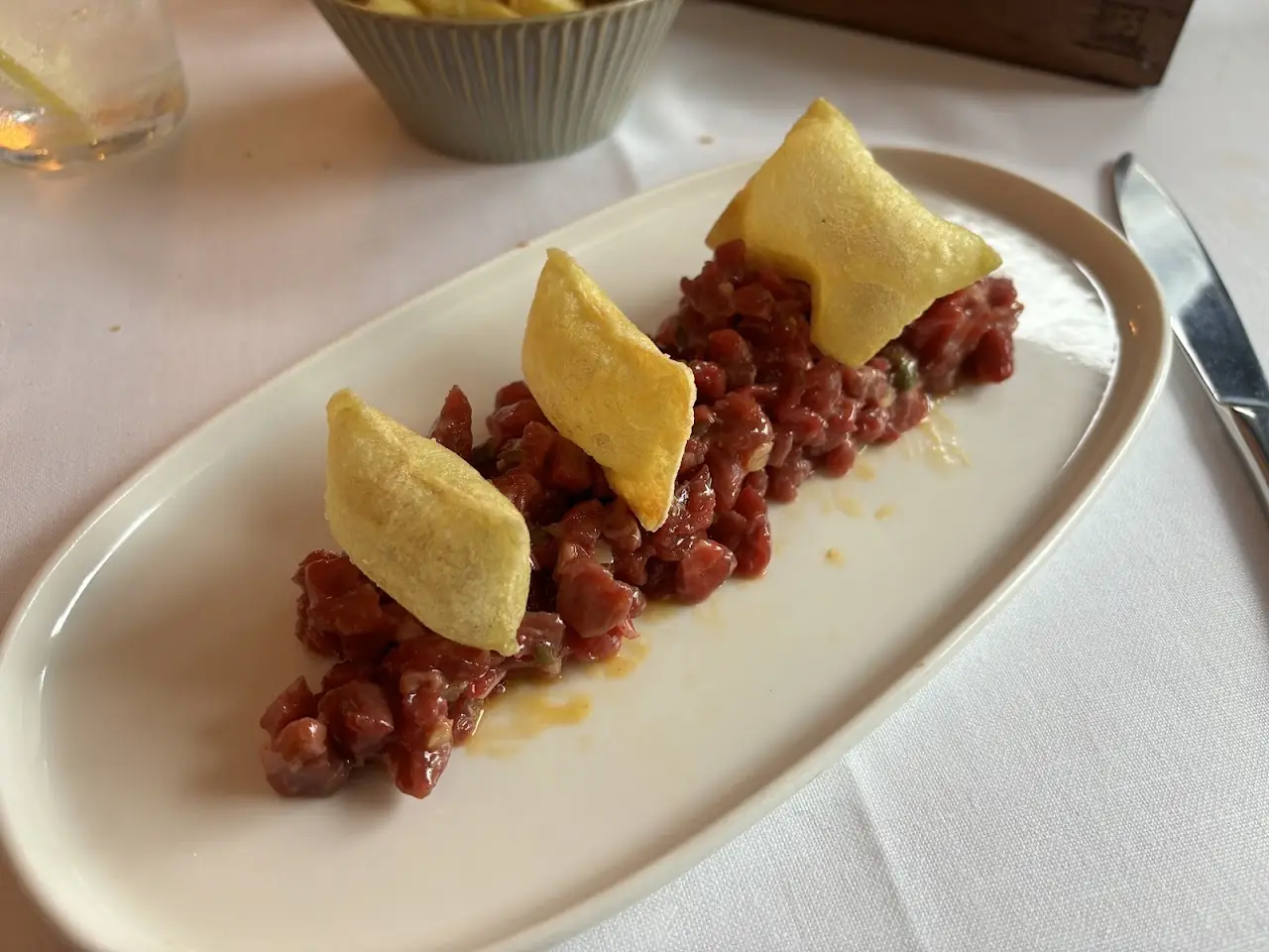 Diced raw tuna tartare on an oval plate with small golden pastry triangles.