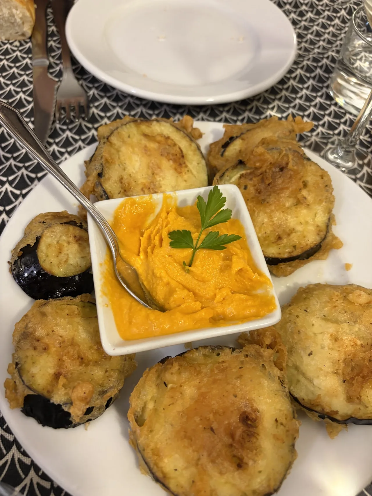 Plate of golden battered fried eggplant slices arranged around a small dish of orange puree garnished with a parsley sprig