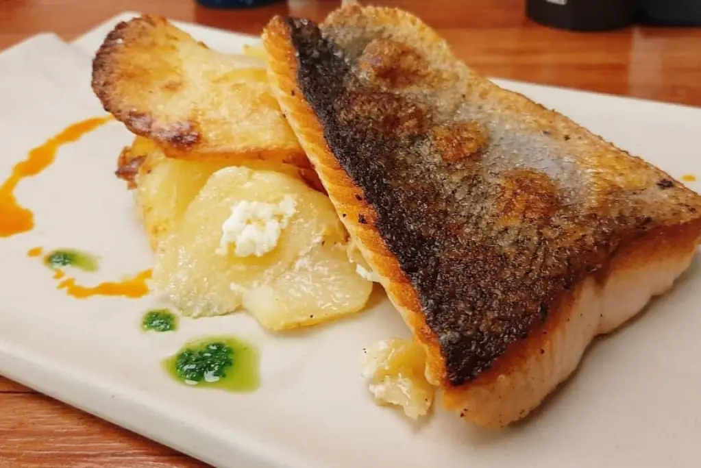 Pan-seared fish fillet with crisp skin, served over sliced potatoes with a dollop of cheese and herb oil drizzle, at Vivant