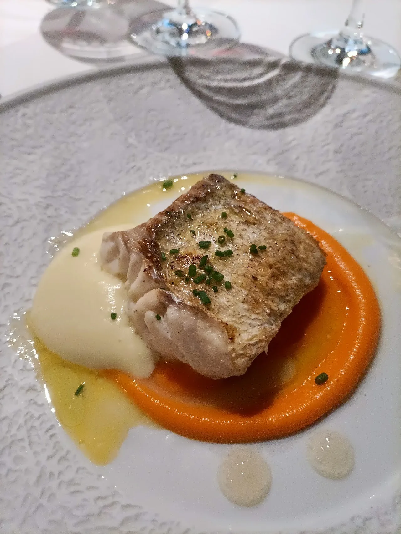 A seared piece of white fish on an orange purée with sauce on a white plate