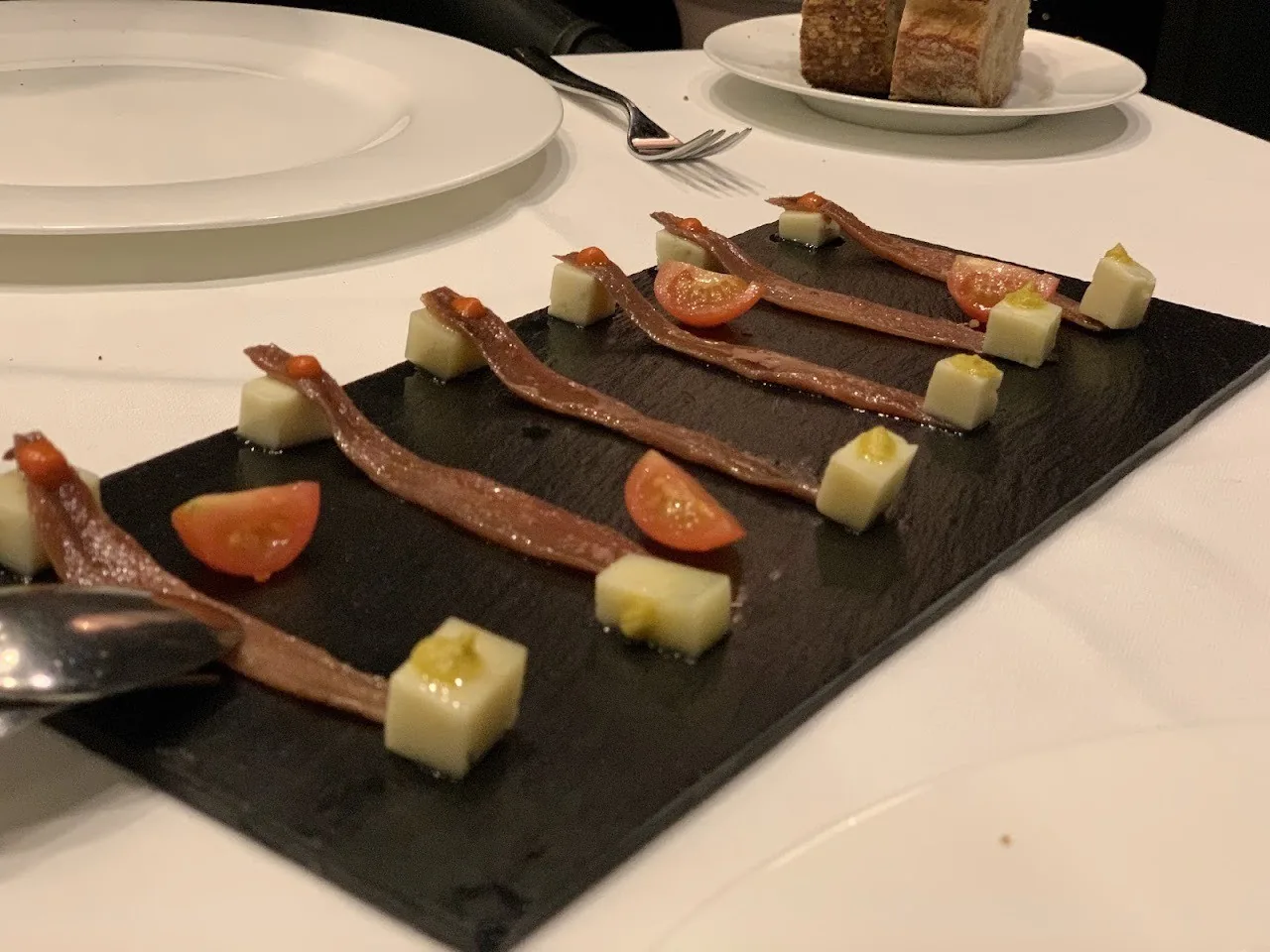 Strips of marinated fish with tomato and cubes of cheese on a slate