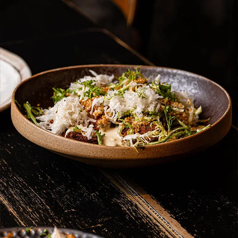Shredded vegetable and herb salad with crispy fried bites in a light sauce, served in a dark ceramic bowl at Vrutal