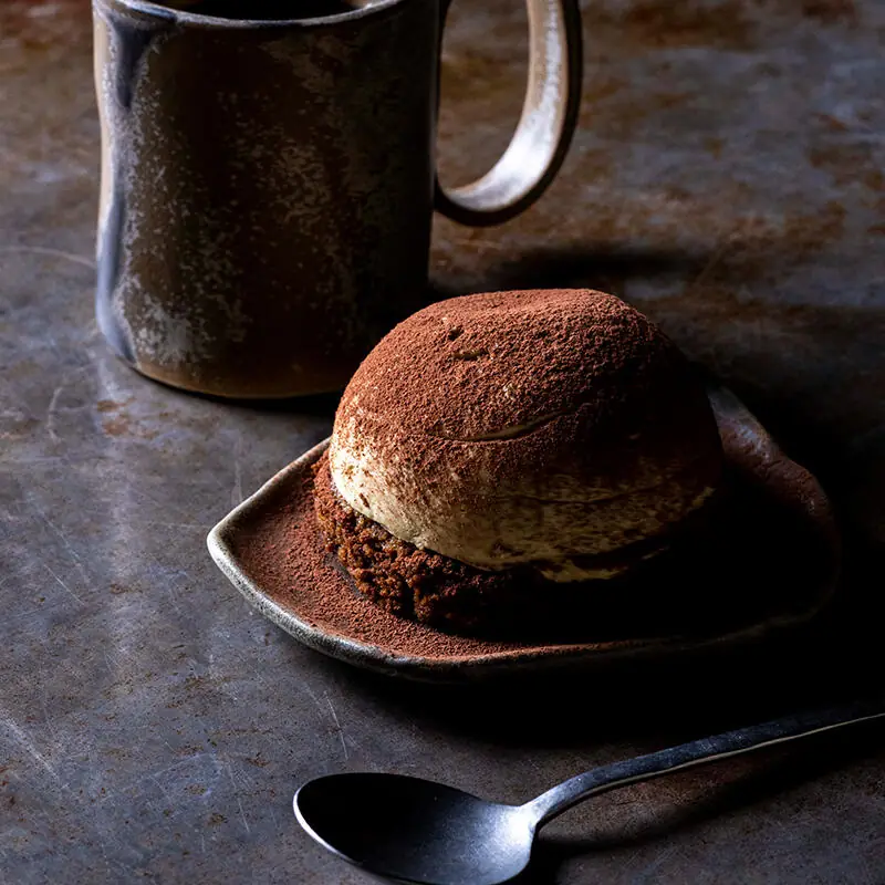 Cocoa-dusted dessert scoop on a small plate beside a ceramic mug and spoon at Vrutal