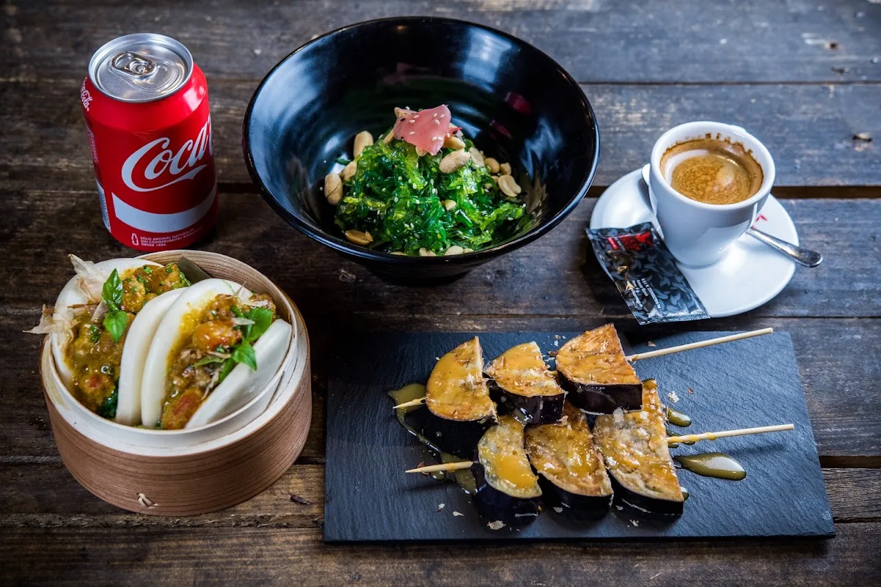 A table spread of noodle salad, steamed buns, skewers, and coffee