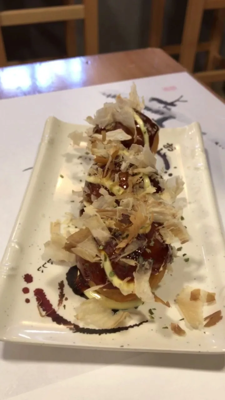 A dish topped with shaved bonito flakes and sauce