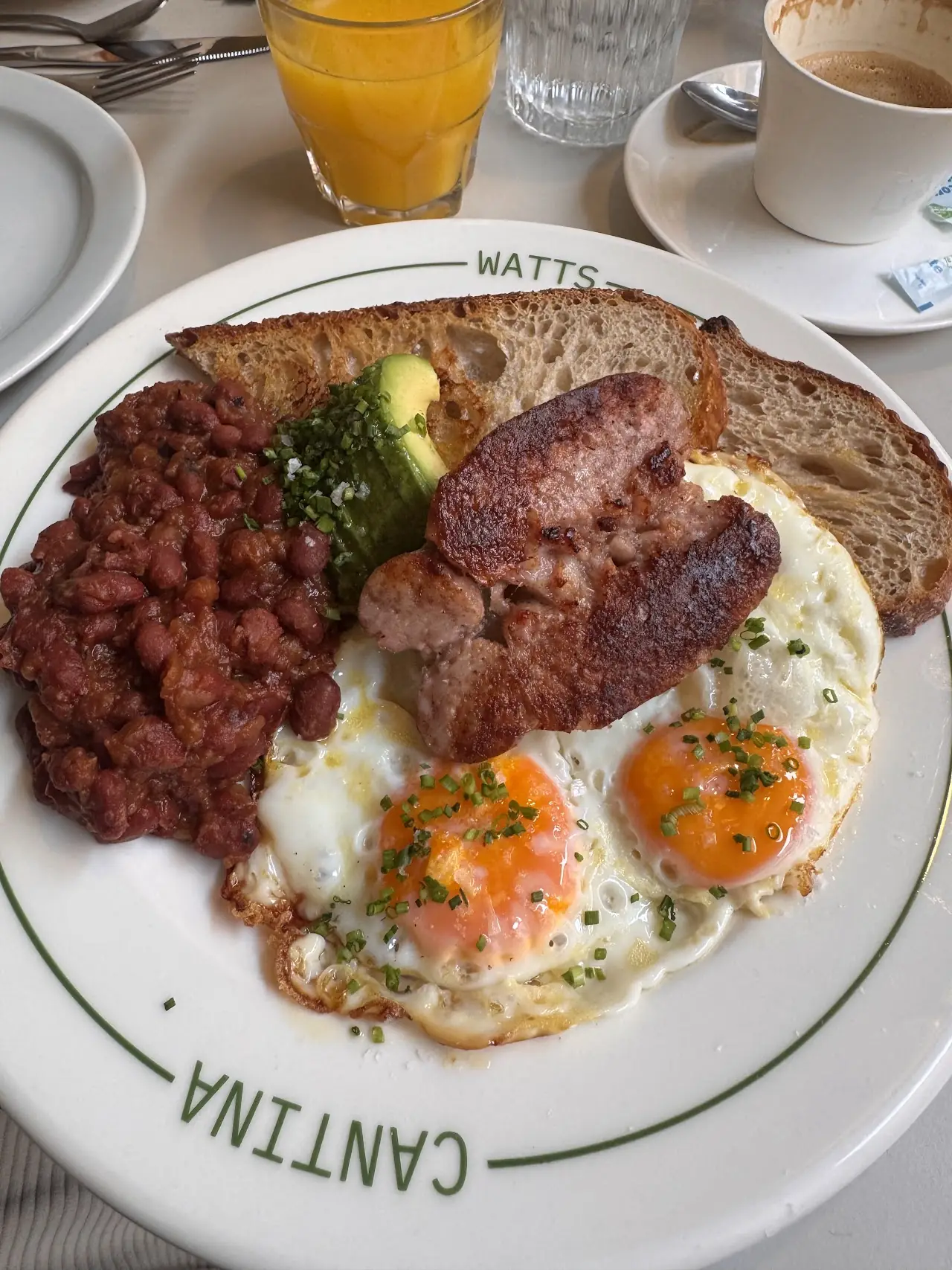Full breakfast of fried eggs, sausage, beans, avocado and toast, with orange juice and coffee