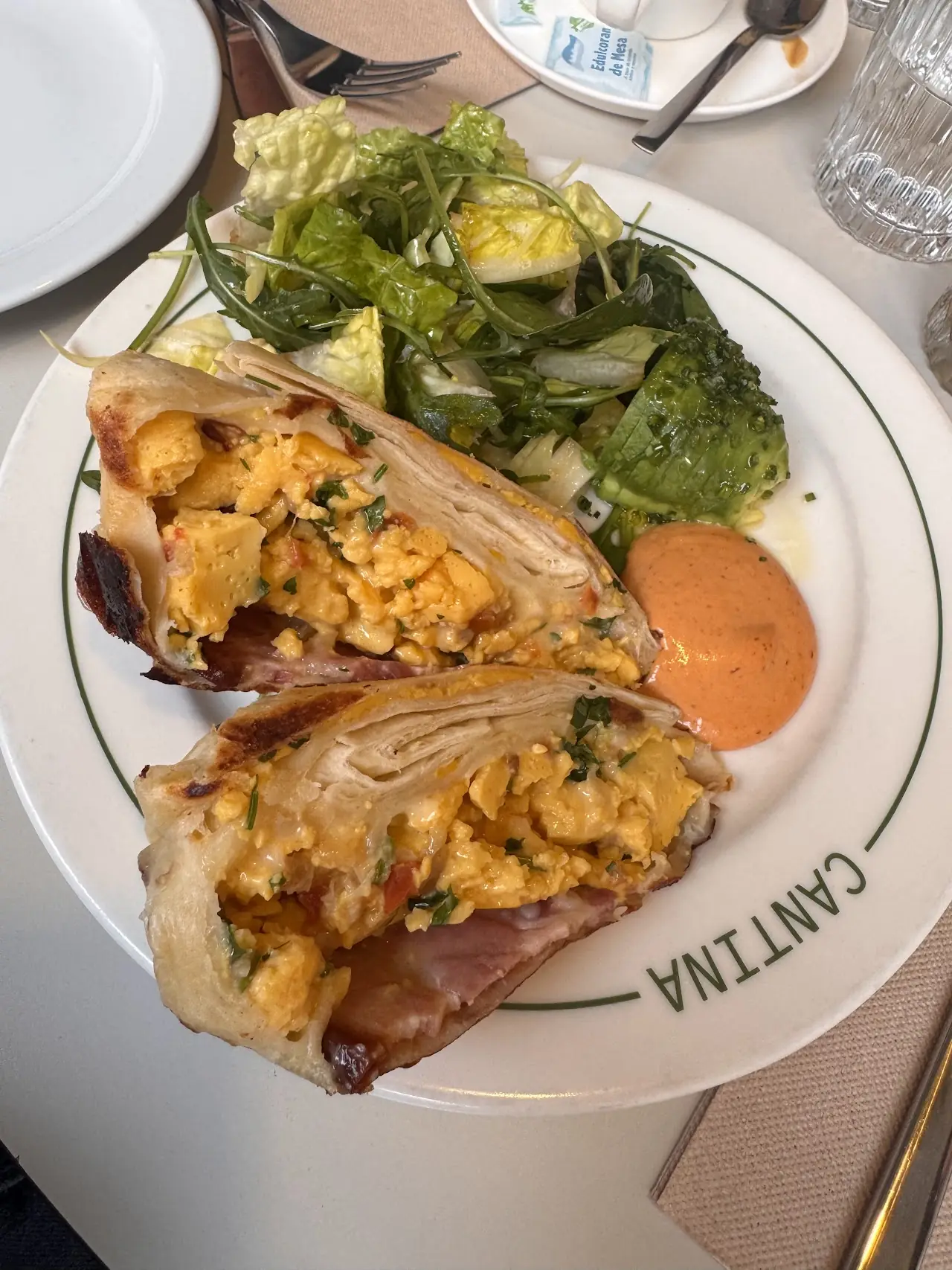 A breakfast burrito filled with scrambled egg, cut in half, with a green salad and a dipping sauce