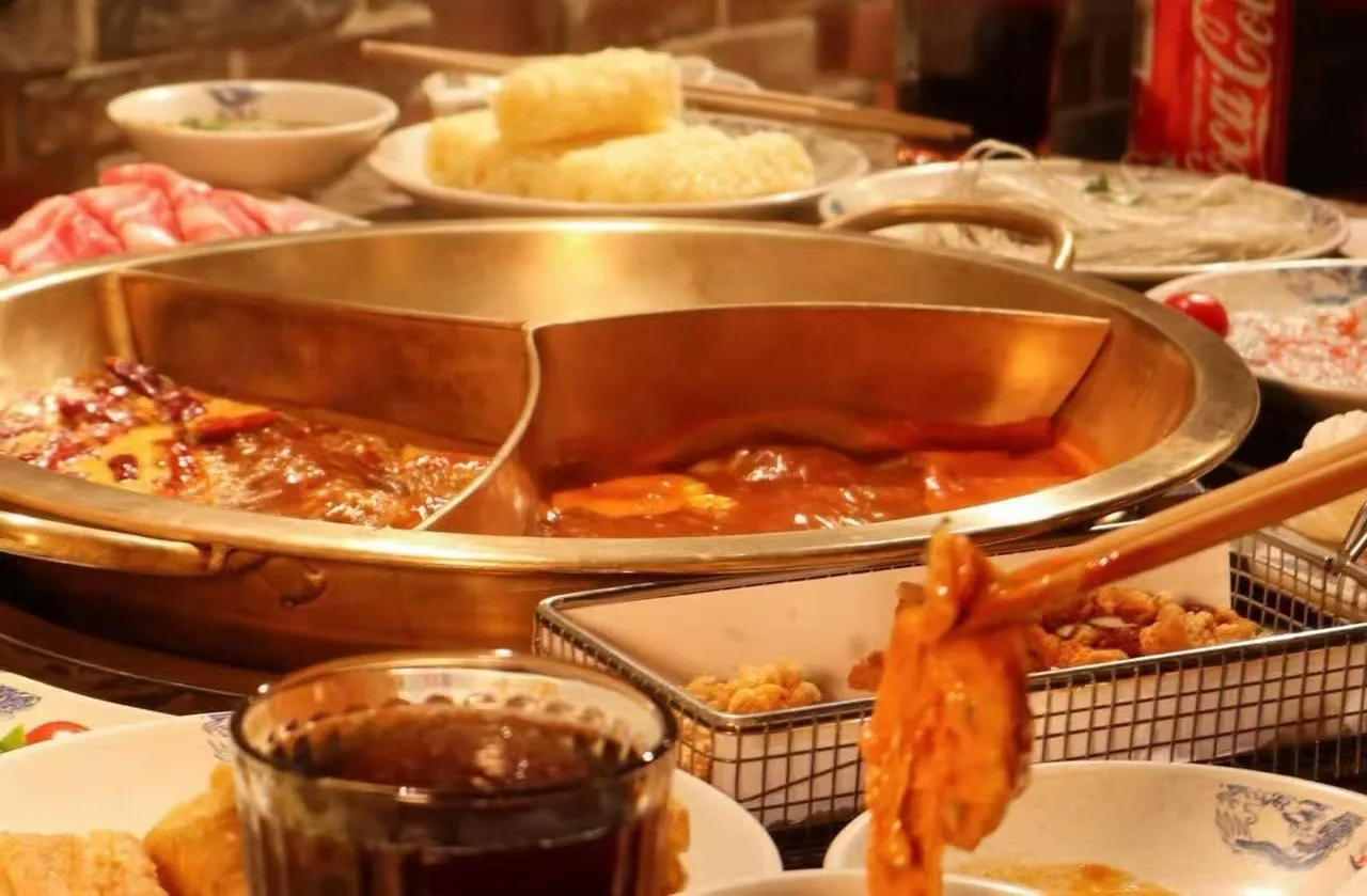 A divided hot pot with red broth and dishes around it
