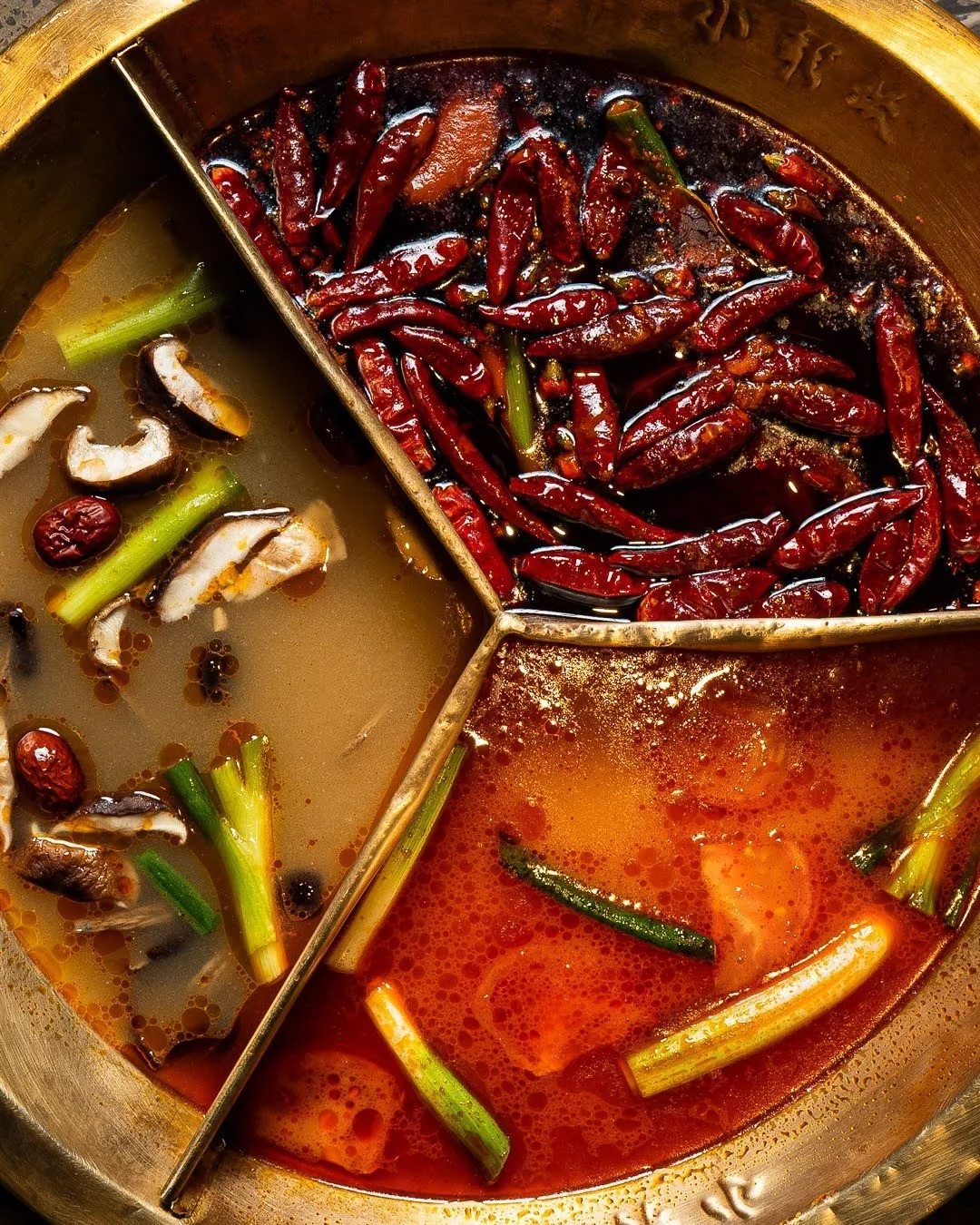 An overhead view of a three-section hot pot with dried chillies and mushrooms