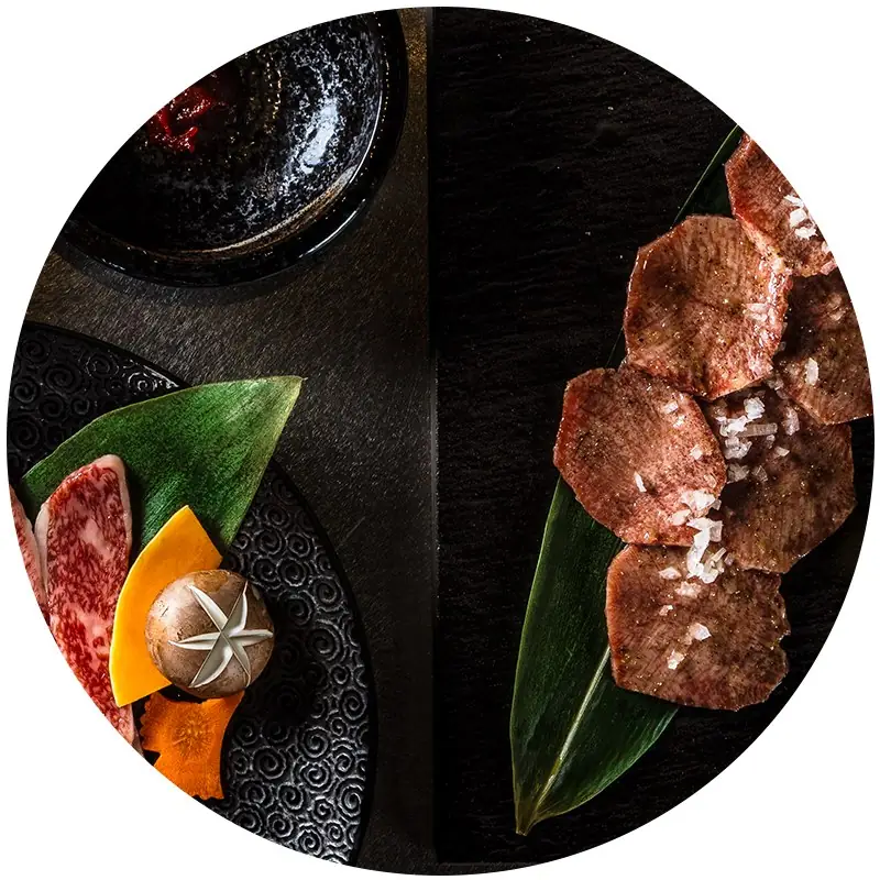 Two dark plates of sliced wagyu beef, one raw with garnish and one with salt-topped slices on a green leaf