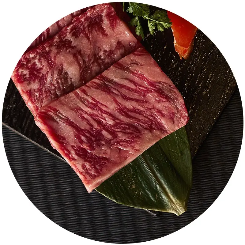 Close-up of two folded slices of heavily marbled raw wagyu beef on a black textured plate with a green leaf