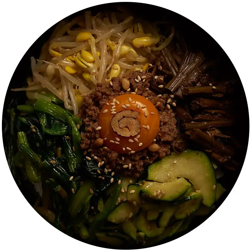 Bibimbap bowl with seasoned ground beef, bean sprouts, greens, sliced zucchini, and an egg yolk topped with sesame seeds