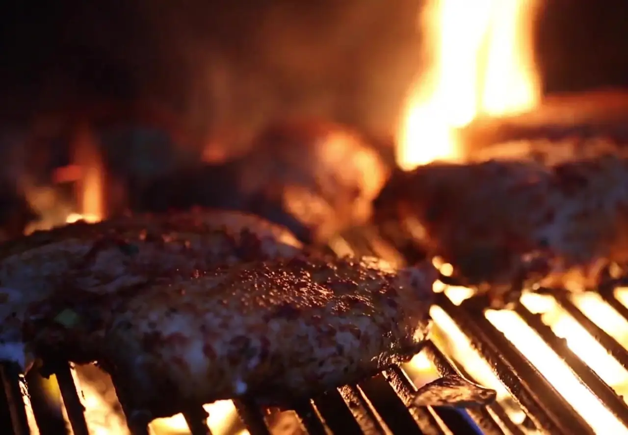 Meat patties grilling over an open flame on a charcoal grill