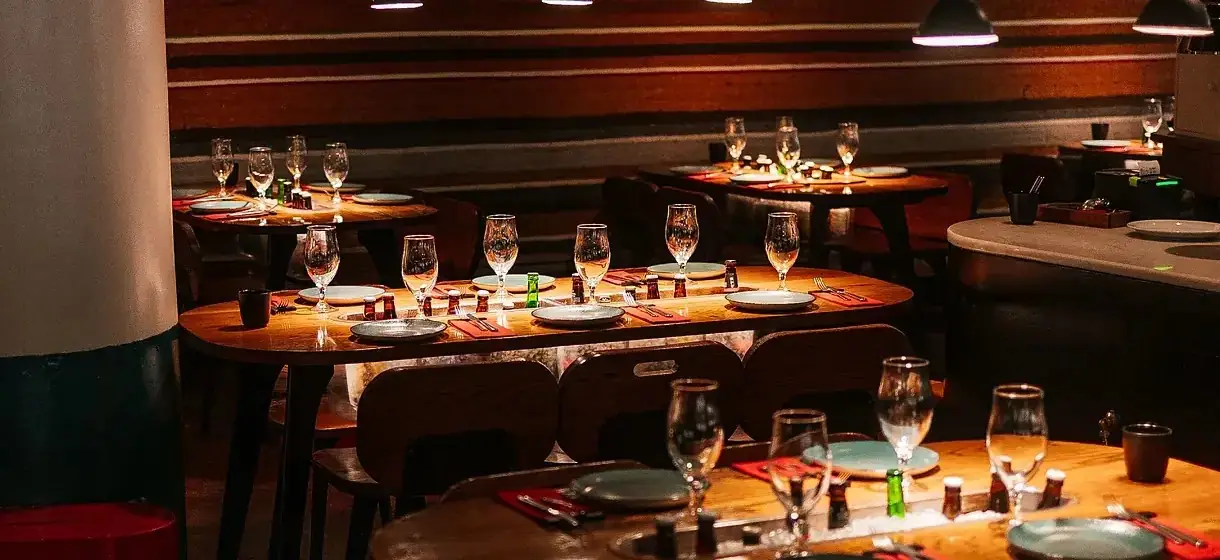 Interior dining room with set wooden tables, wine glasses and hanging pendant lamps against striped panelling