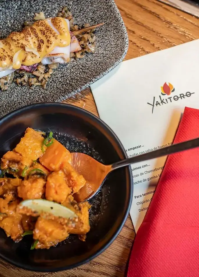 Grilled squid skewer over black rice and a bowl of glazed diced pumpkin with lime, beside a Yakitoro menu card