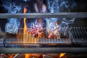 Meat skewers grilling over flames and coals with rising smoke