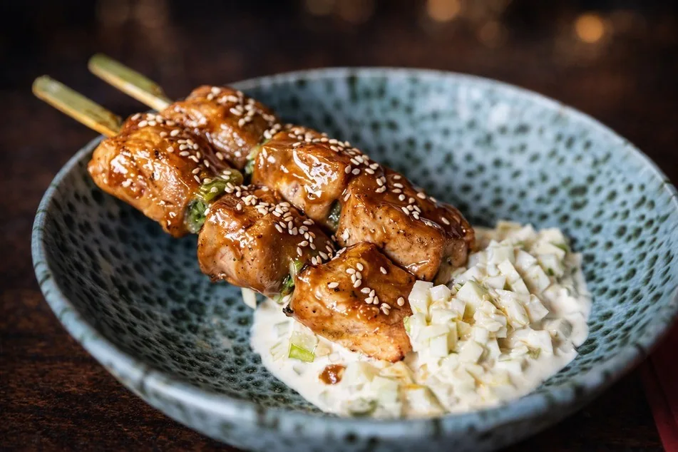Glazed skewered meat sprinkled with sesame in a speckled blue bowl