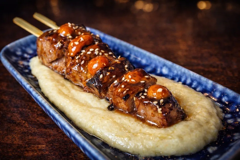 A glazed skewer on a creamy puree on a blue plate