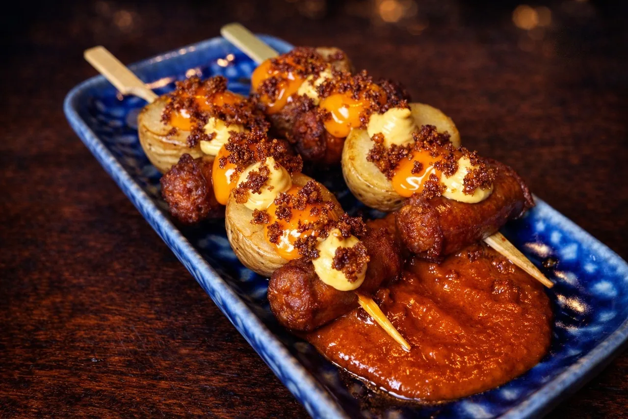 Two grilled skewers on a blue tray with a red sauce