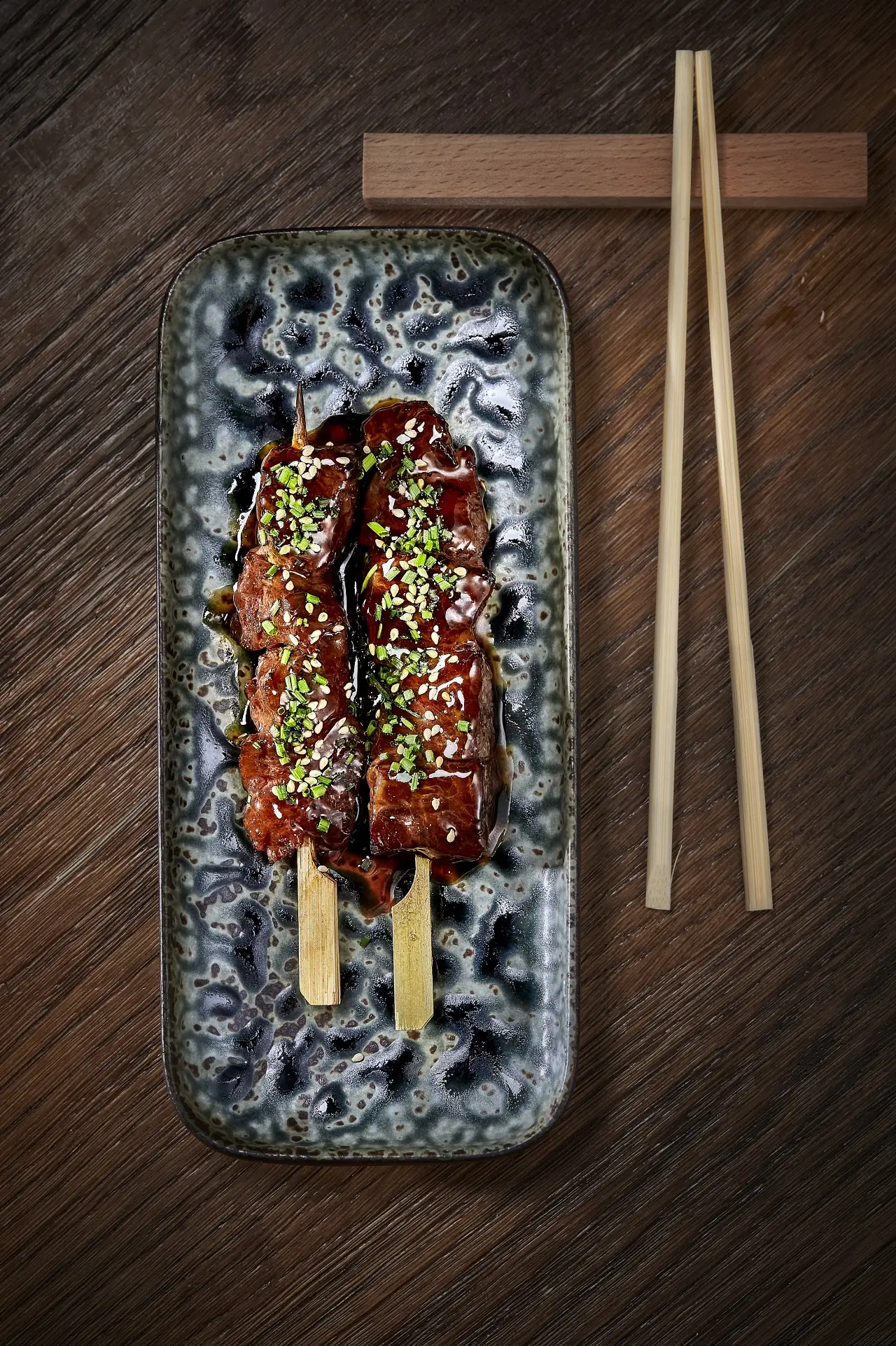 Grilled skewer glazed in sauce and topped with sesame seeds served with chopsticks