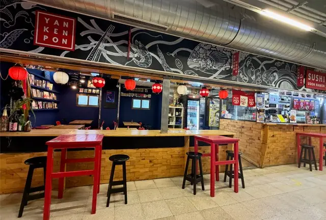 Interior bar area with red high tables and black stools, red paper lanterns, a food counter and a YAN KEN PON wall logo