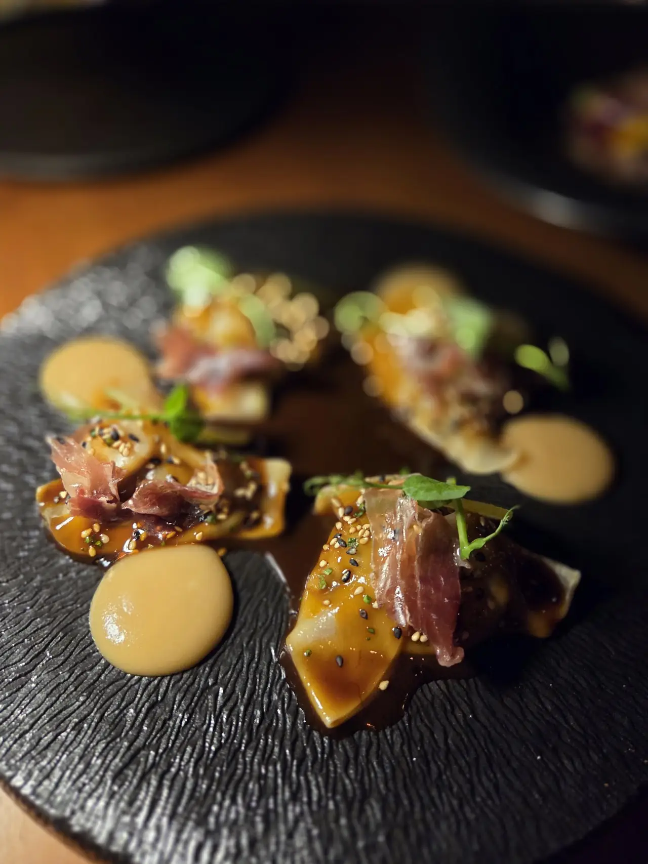 Seared tuna bites with sesame seeds and dots of sauce on a dark slate.