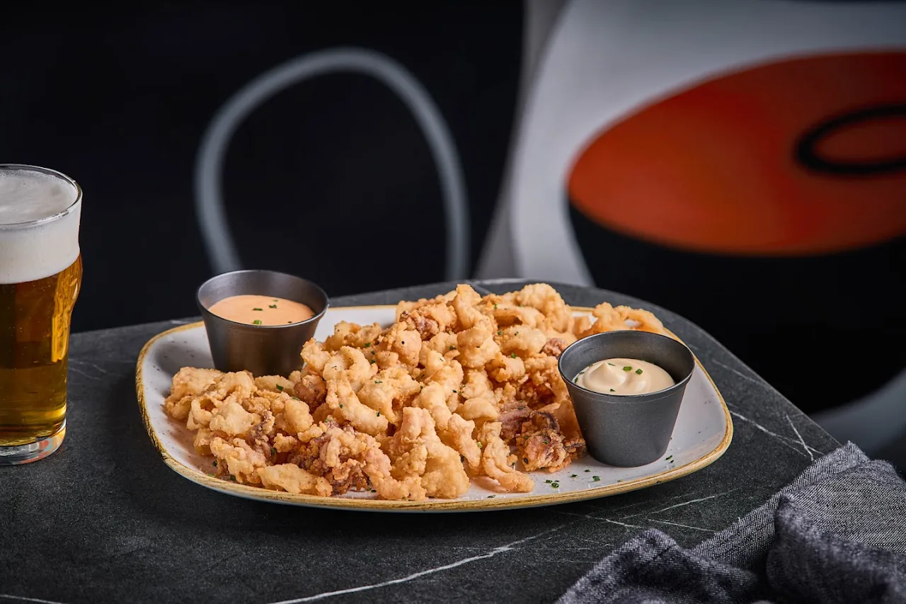 A platter of crispy fried tempura-style strips with two dipping sauces and a beer