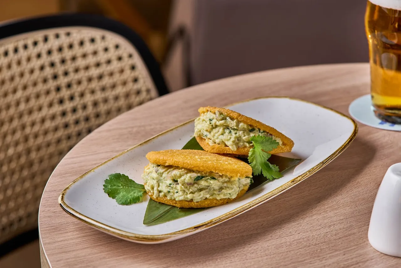 Two halves of a green-hued sandwich on a white plate with a beer