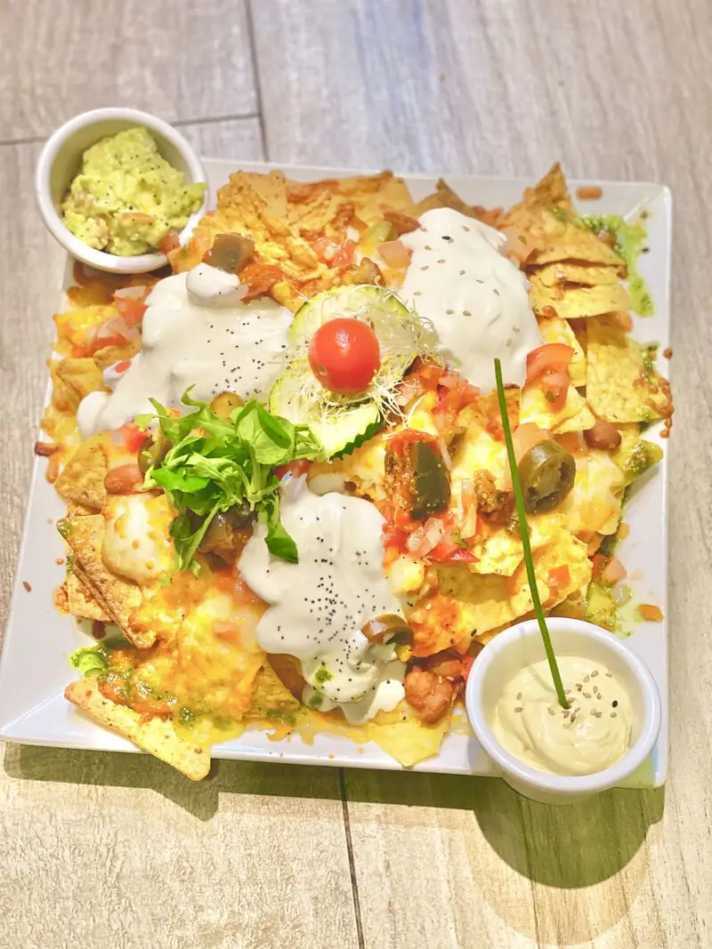 Loaded nachos with melted cheese, jalapenos, tomato and white sauce, served with bowls of guacamole and aioli on a square plate