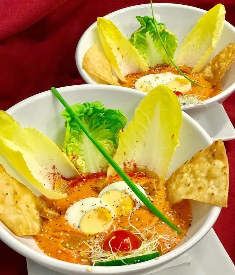 A white bowl of salad with chicory leaves, egg and a red sauce