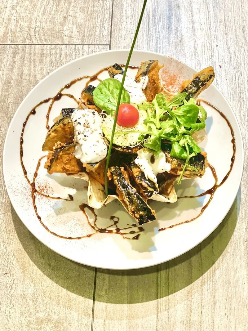 A white plate of a vegetable dish with sauce and a green garnish