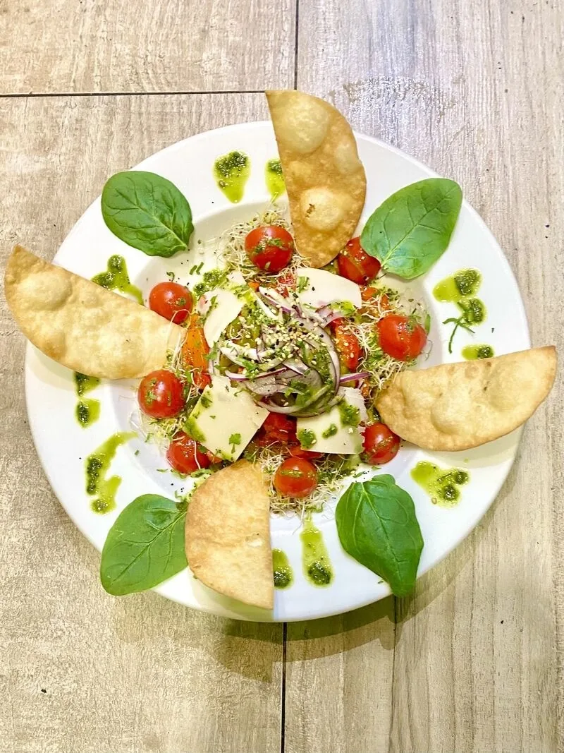 A plate of spinach leaves with tomatoes, crisps and creamy pieces drizzled with green oil