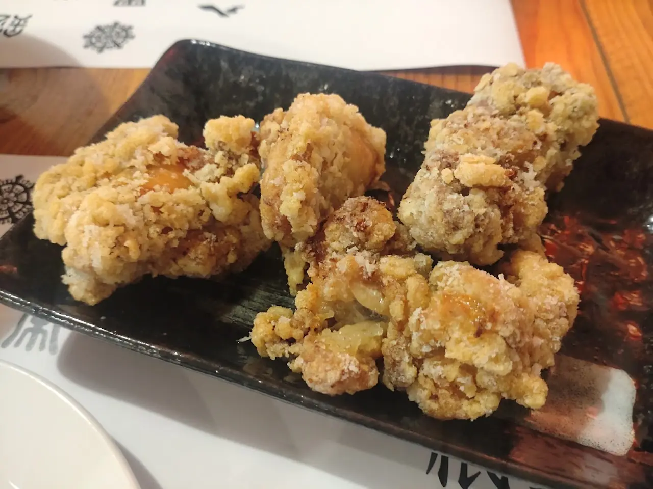 Japanese-style karaage fried chicken pieces on a black plate, at Yoi Yoi Gion.
