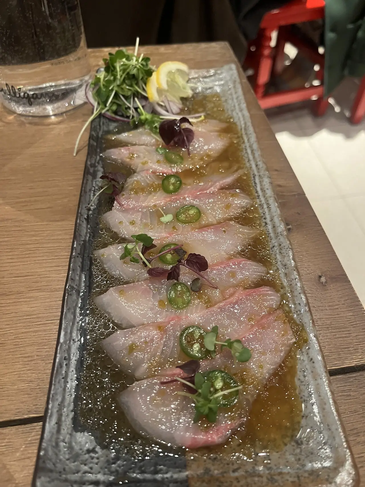 Sashimi slices arranged on a rectangular plate with citrus and herb garnish
