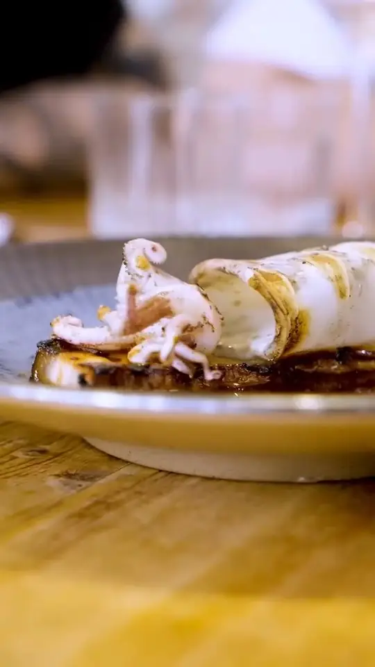 Grilled whole squid with tentacles plated over charred vegetables