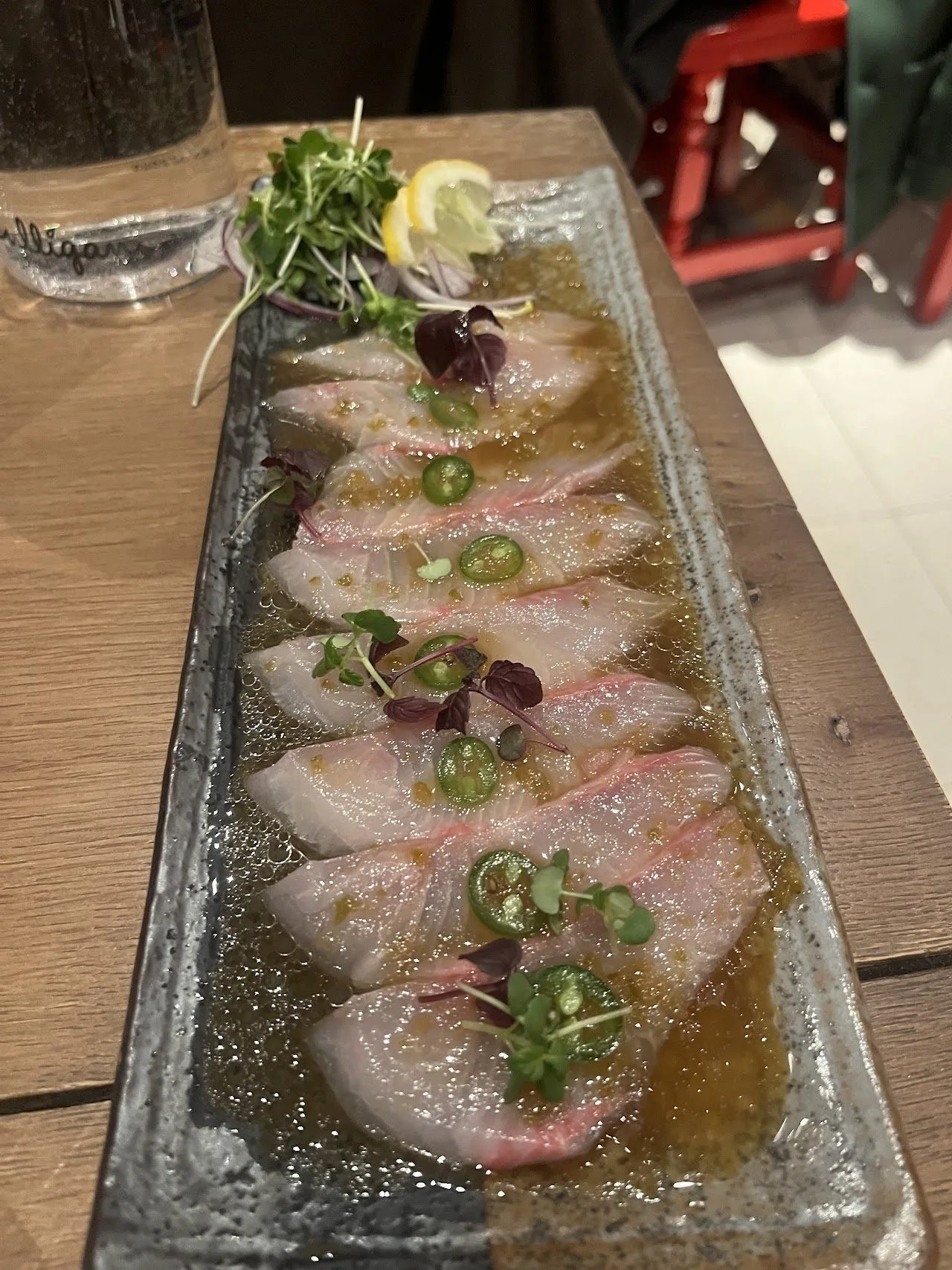 Thin slices of white fish topped with green chilli slices on a long glass plate