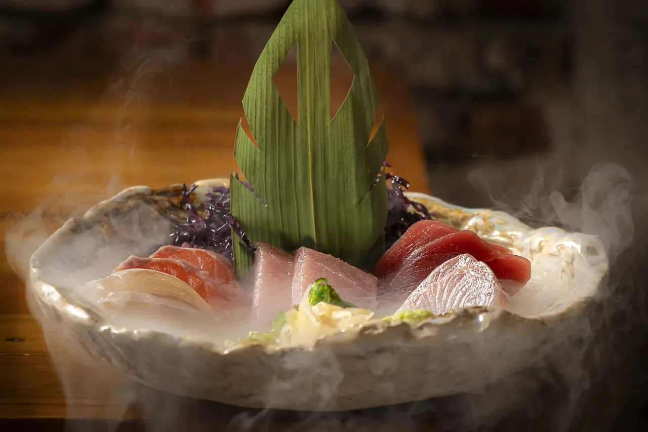 A rustic bowl of sashimi slices with a bamboo leaf garnish and rising smoke