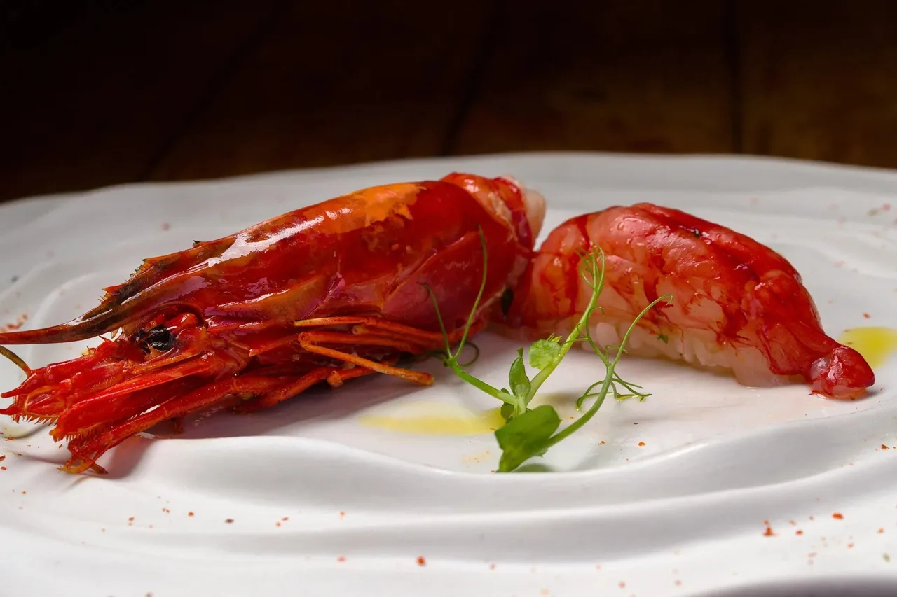 A white plate with two red prawns and small green garnishes
