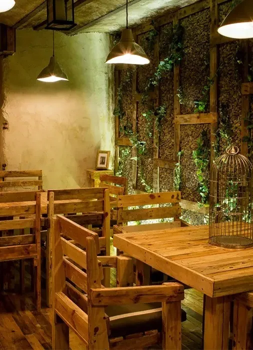 A corner with wooden pallet-style tables and chairs beside a wall covered in climbing plants