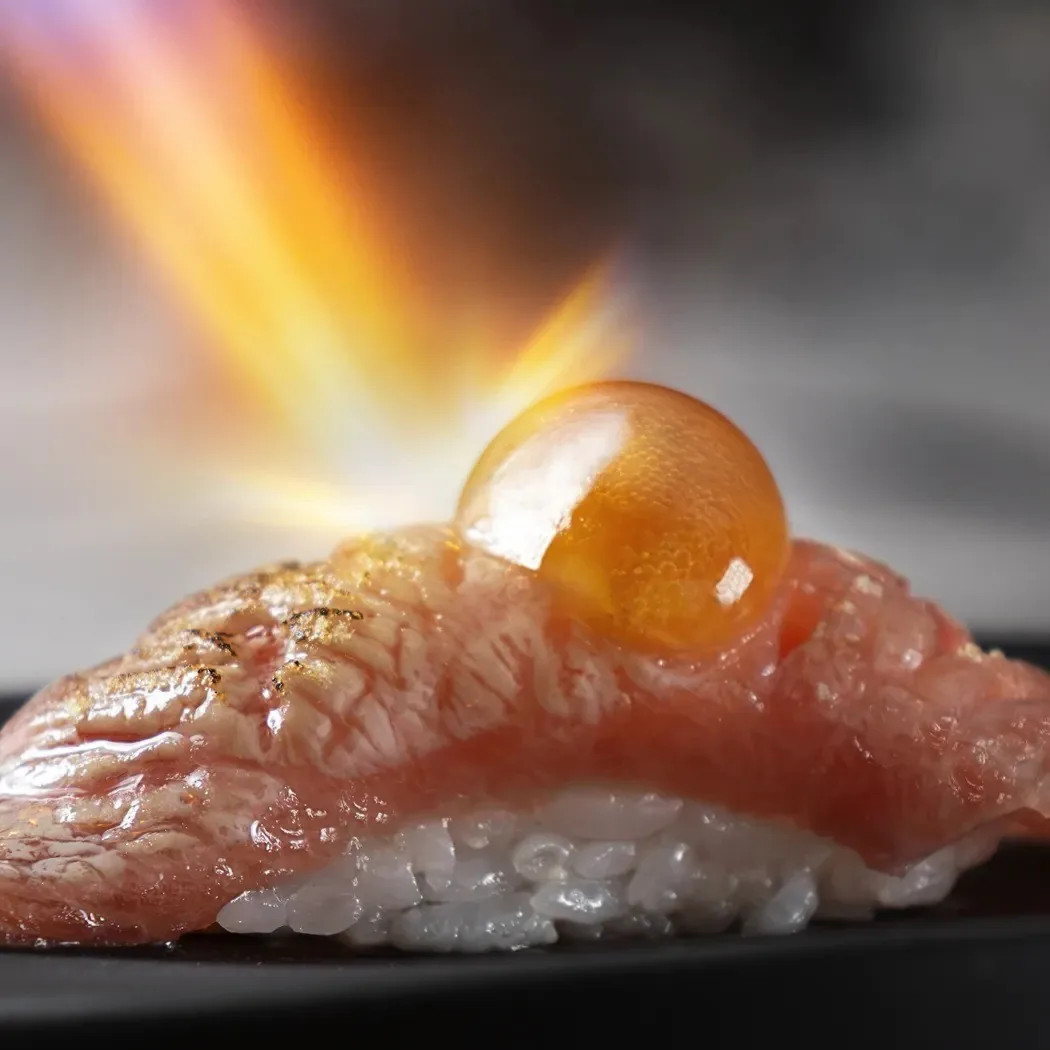 Nigiri with red fish being torched, with a golden drop on top