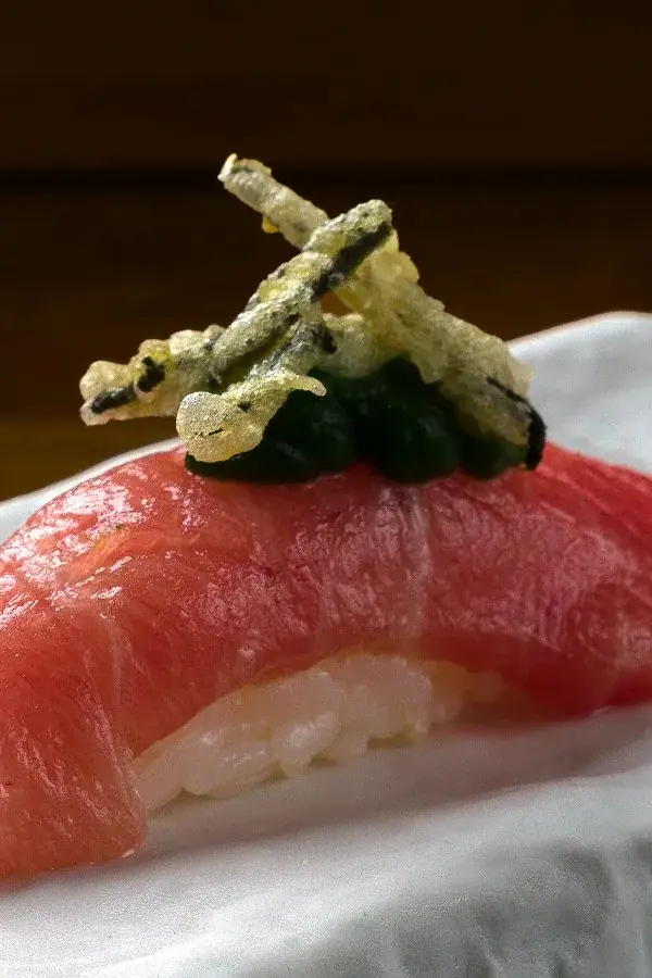 Close-up of tuna nigiri topped with fried garnish and dark roe