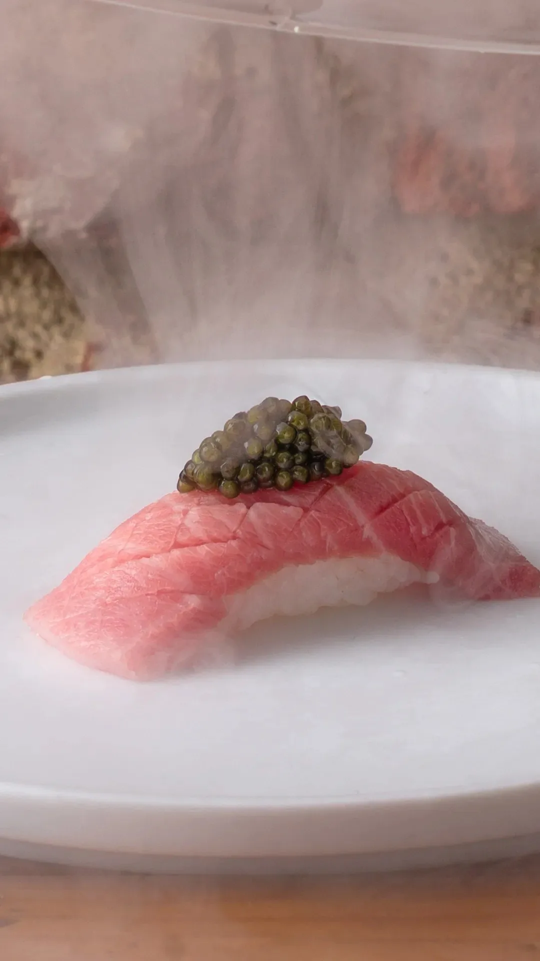 A nigiri topped with pink fish and dark caviar on a white plate
