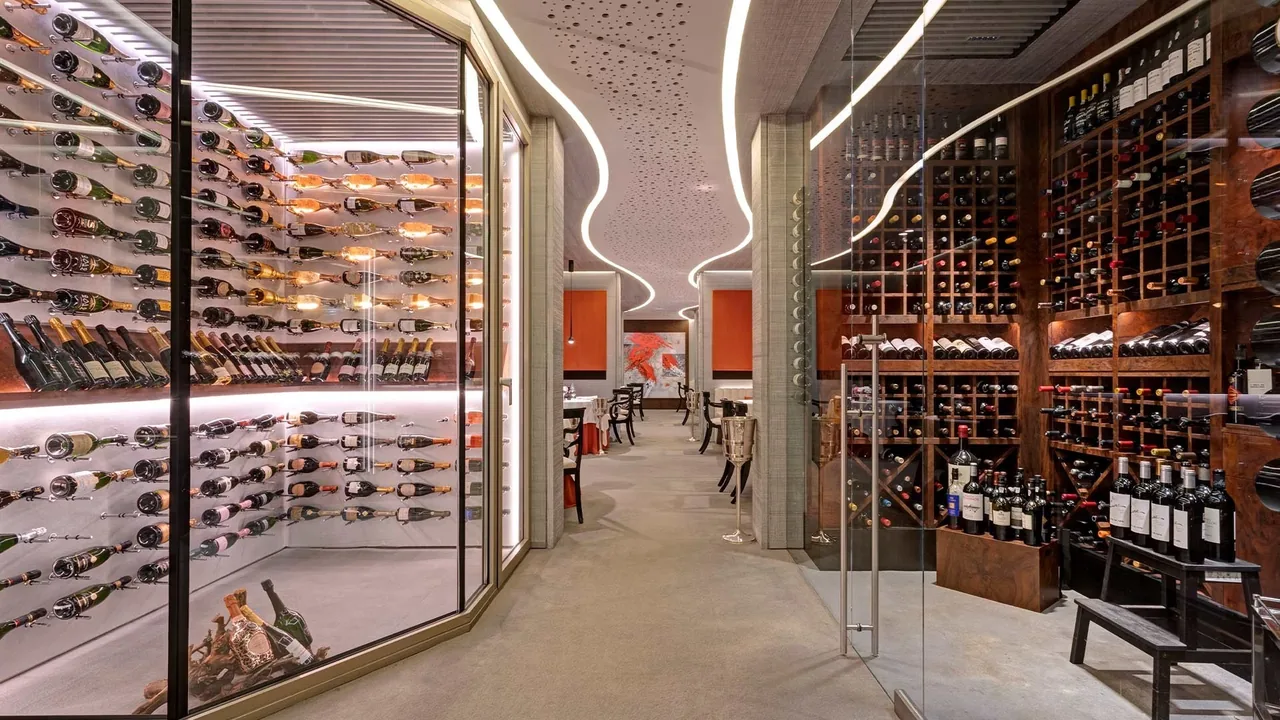 A glass-walled wine cellar with racks of bottles along a curved corridor.