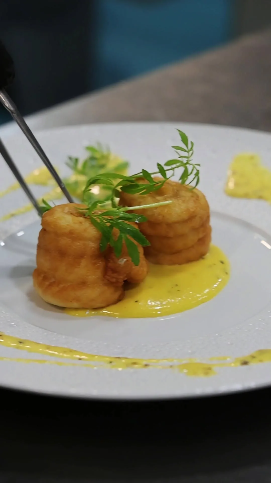 Two golden round croquette-style bites in a yellow sauce on a white plate.