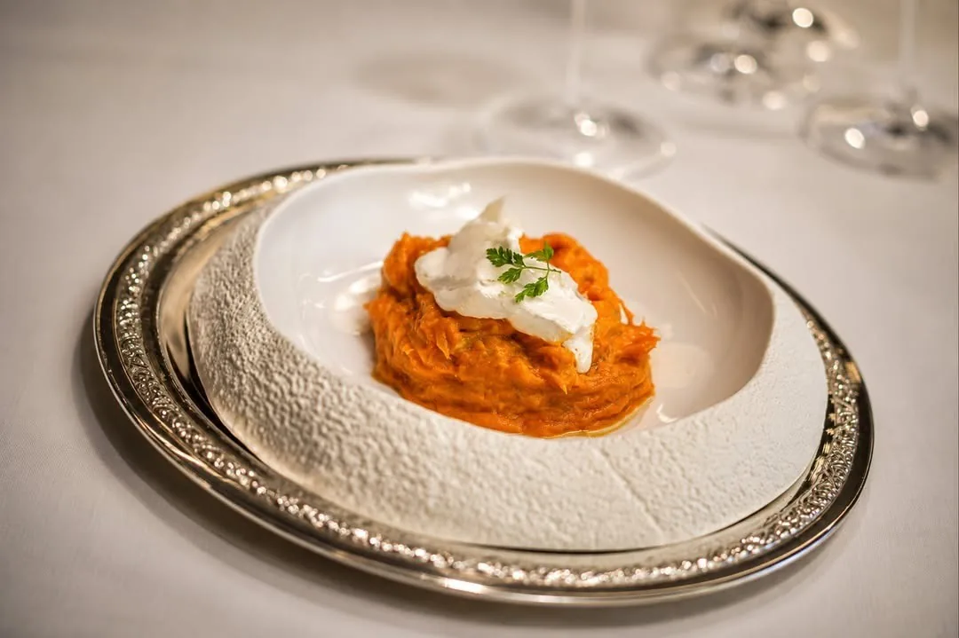 A textured white plate with an orange purée topped with cream