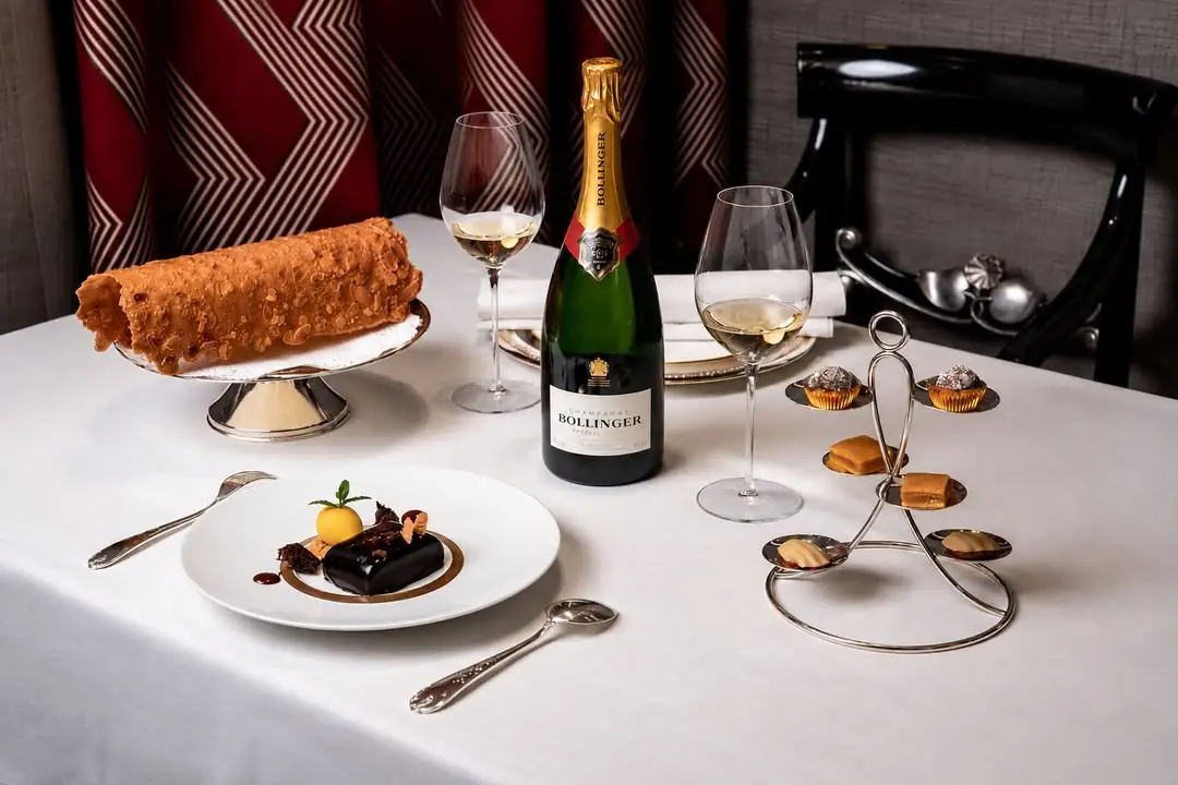 Table spread with a chocolate dessert plate, poured champagne glasses, Bollinger bottle and petit fours on a stand