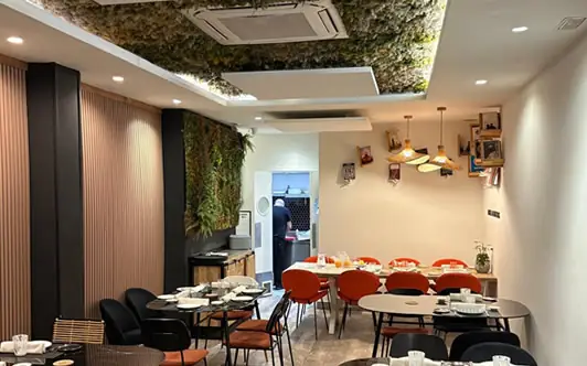 Dining room with round tables set for service, orange and black chairs, a living moss ceiling panel and a green vertical plant wall