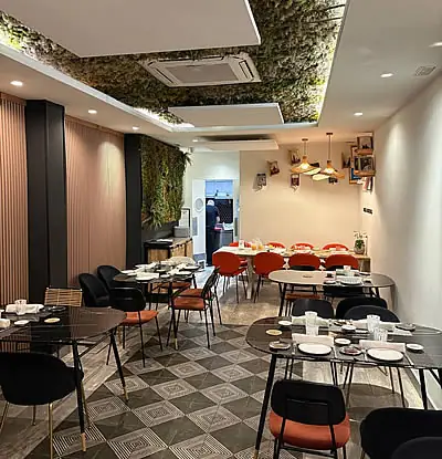 Dining room with black and orange chairs, checkered tiled floor, moss ceiling panel and green plant wall