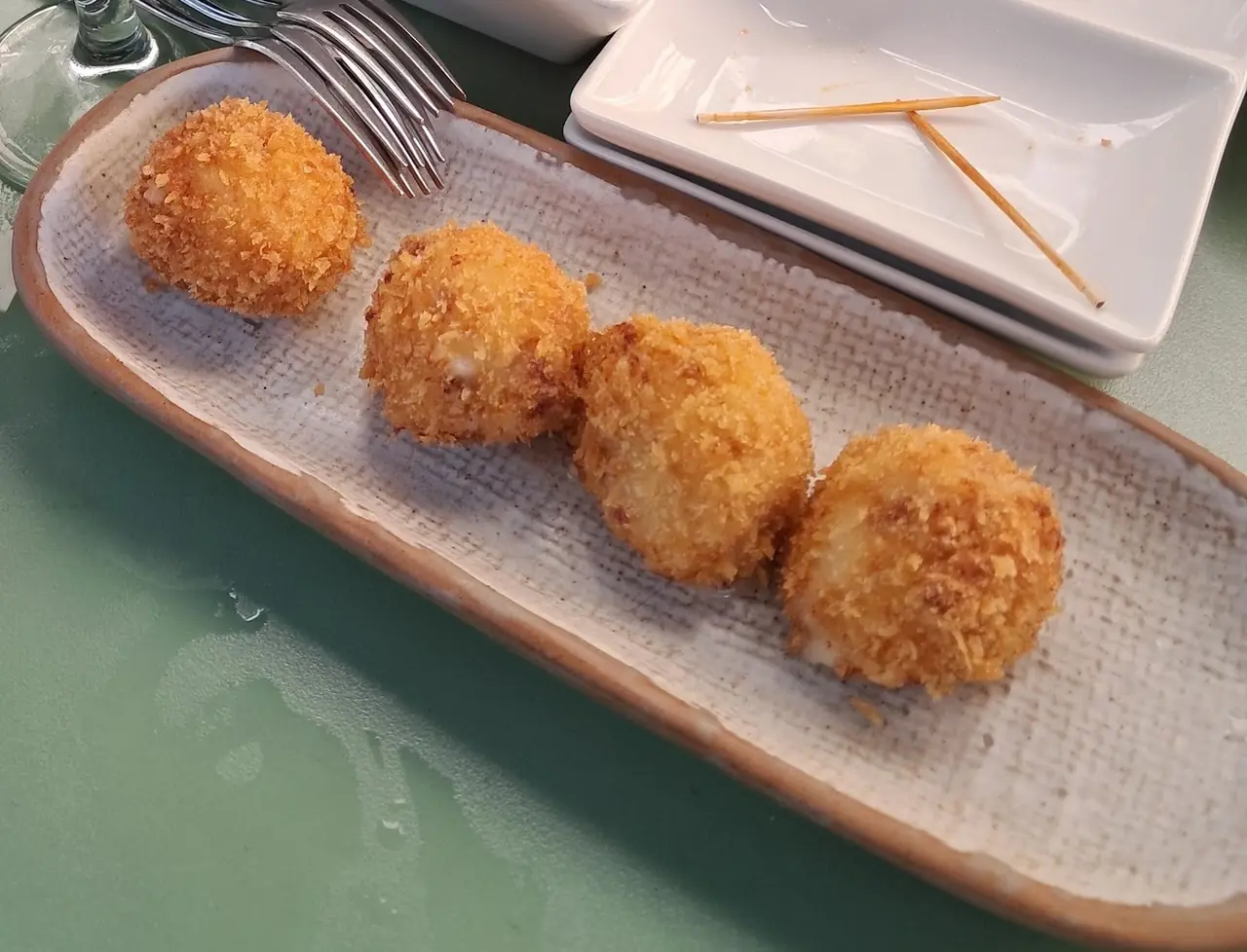 Four crisp, crumbed croquetas on a long ceramic tray