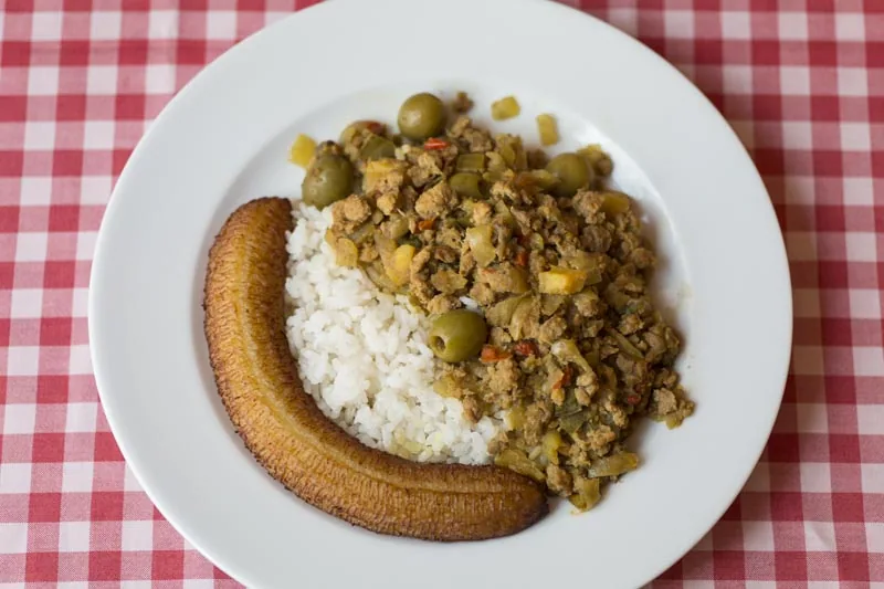 A plate of ground beef picadillo with green olives, white rice, and fried plantain
